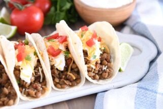 Three tacos of flour tortillas filled with cooked lentils, sour cream, cheese and tomatoes.