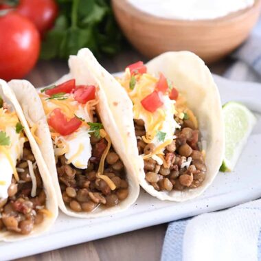Three tacos of flour tortillas filled with cooked lentils, sour cream, cheese and tomatoes.