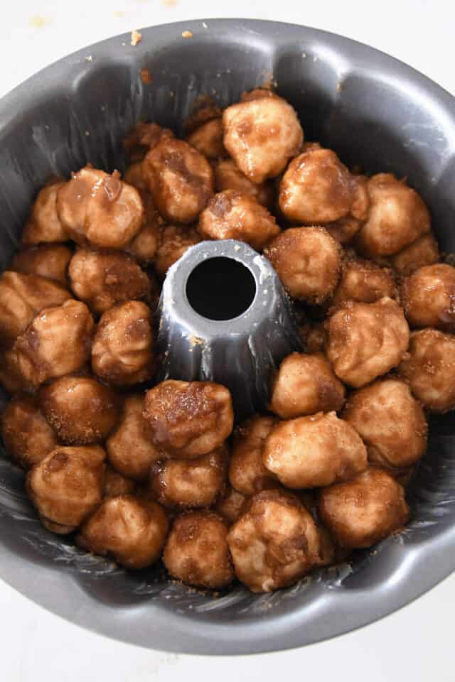 Balls of dough coated in butter and cinnamon and sugar in bundt pan.