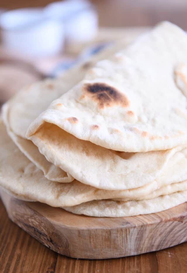 Folded flatbread on top of stack of other flatbread on wood cutting board.