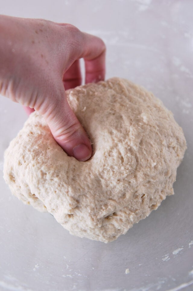Pressing thumb into ball of flatbread dough in glass bowl.