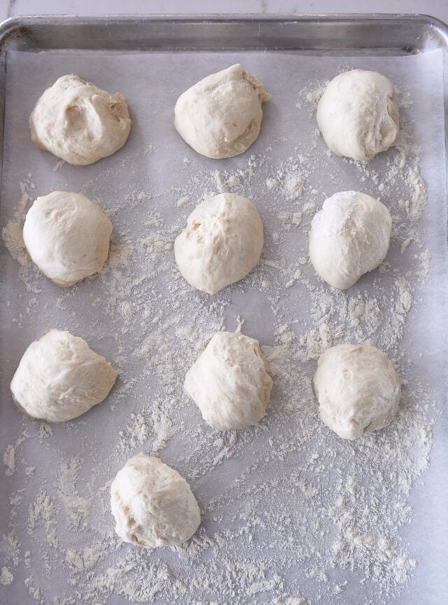 Ten sourdough flatbread dough balls on floured parchment lined baking sheet.