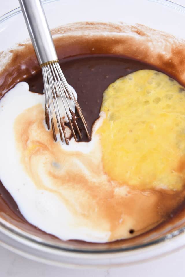 Adding buttermilk and eggs to chocolate cake batter.