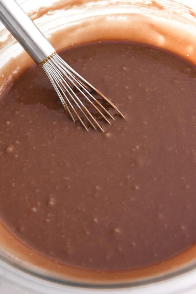 Whisking chocolate cake batter in glass bowl.