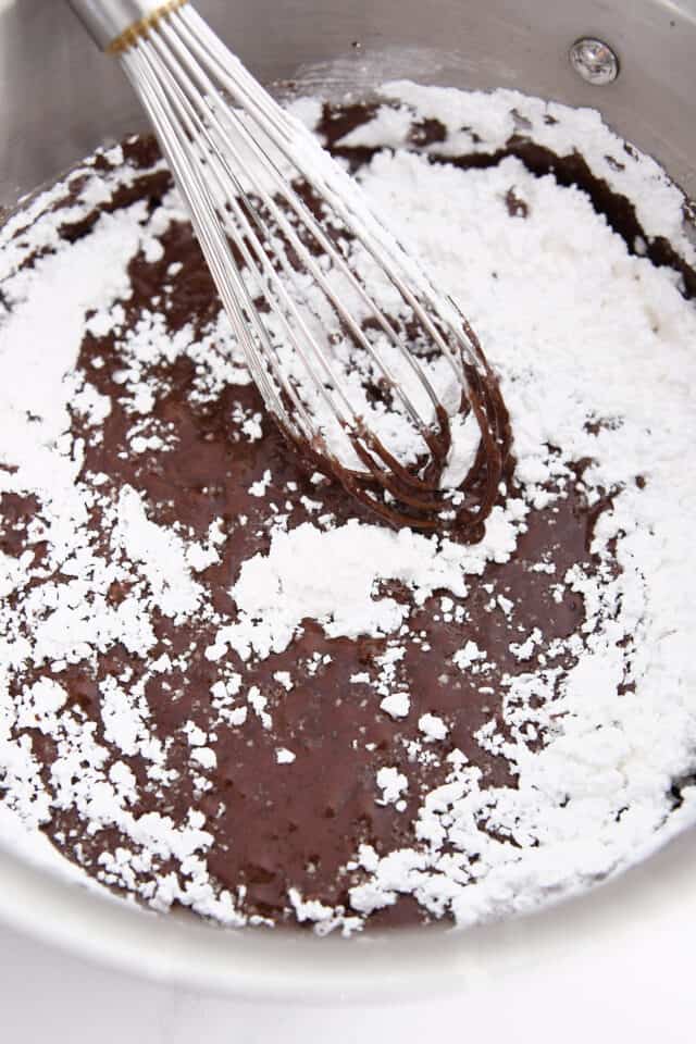 Whisking powdered sugar into melted cocoa and butter in saucepan.