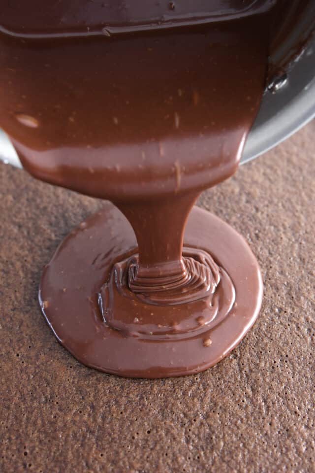 Pouring warm frosting over chocolate sheet cake.
