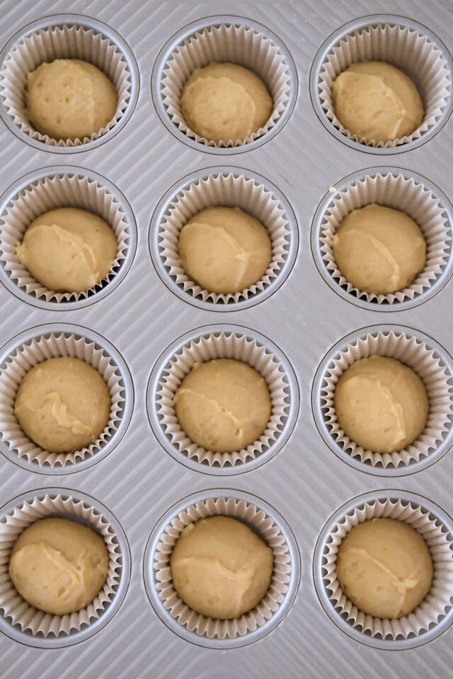 Muffin batter filling half of 12 muffin cups with liners.