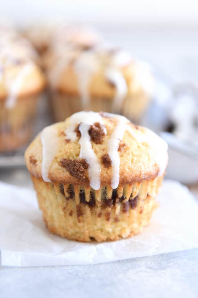 Unwrapped cinnamon roll muffin on parchment paper with glaze drizzled on top.