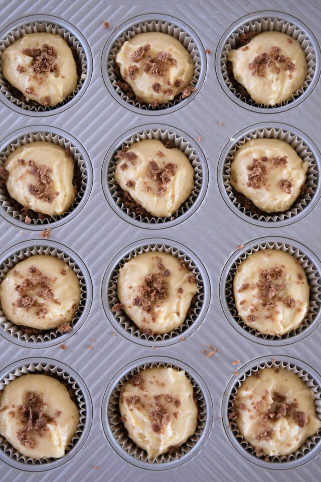 Twelve unbaked muffins topped with batter and cinnamon streusel.