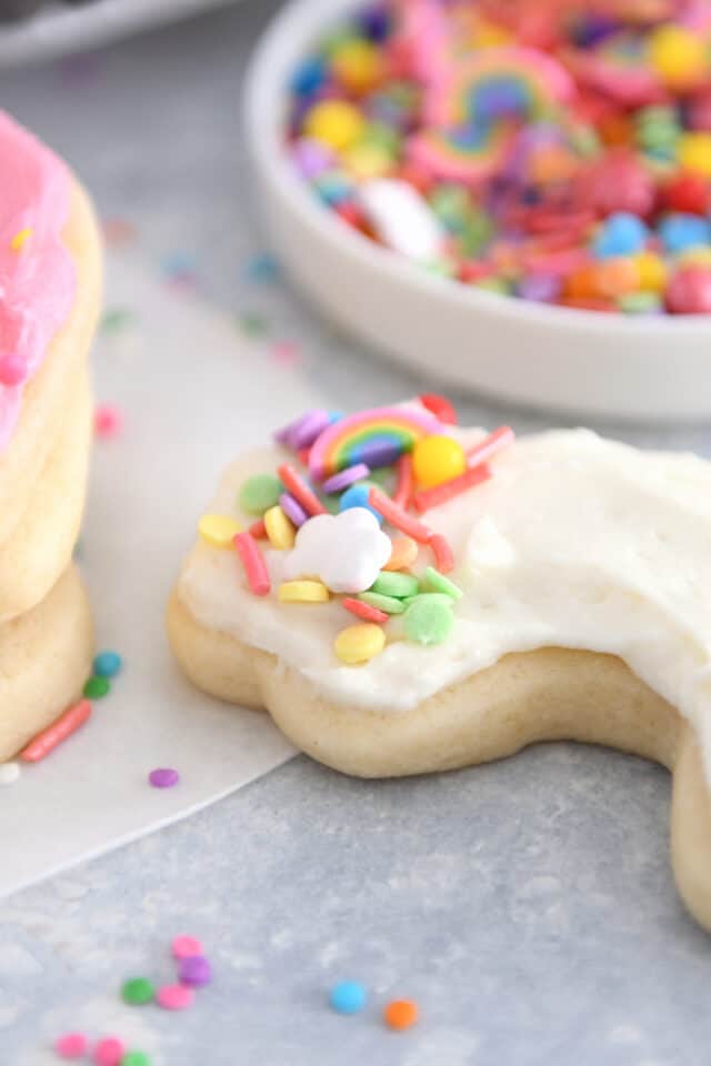 Rainbow shaped sugar cookie frosted with white frosting and colorful sprinkles.
