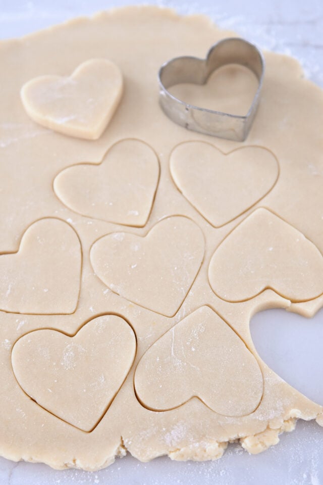 Sheet of sugar cookie dough with heart shaped cookies cutout.