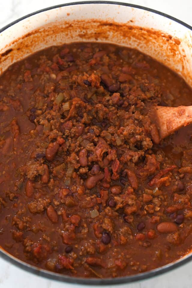 Cooked red chili with beans and ground beef in cast iron pot.