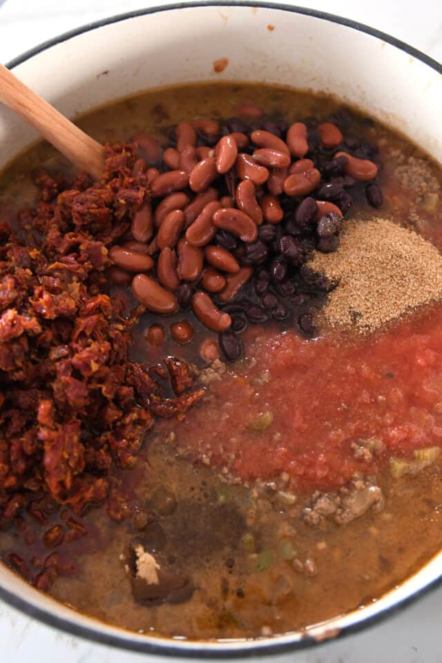 Beef broth, crushed tomatoes, black beans, kidney beans, and sun-dried tomatoes in cast iron pot.