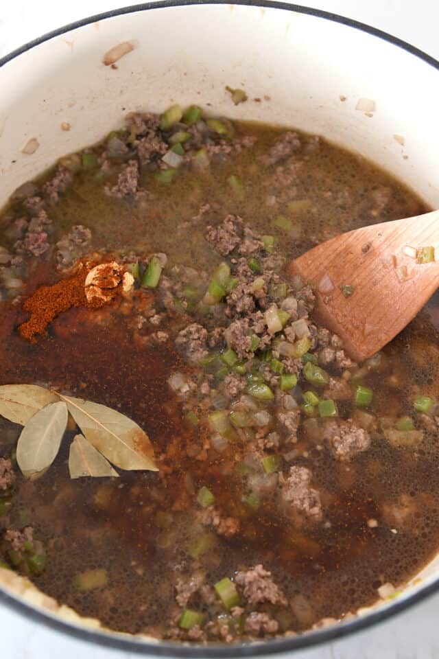 Cast iron pot with cooked ground beef, chili powder, bay leaves and celery.