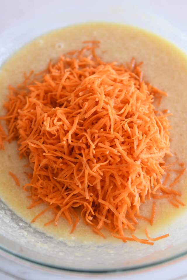 Shredded carrots added to gl، bowl with cake batter.