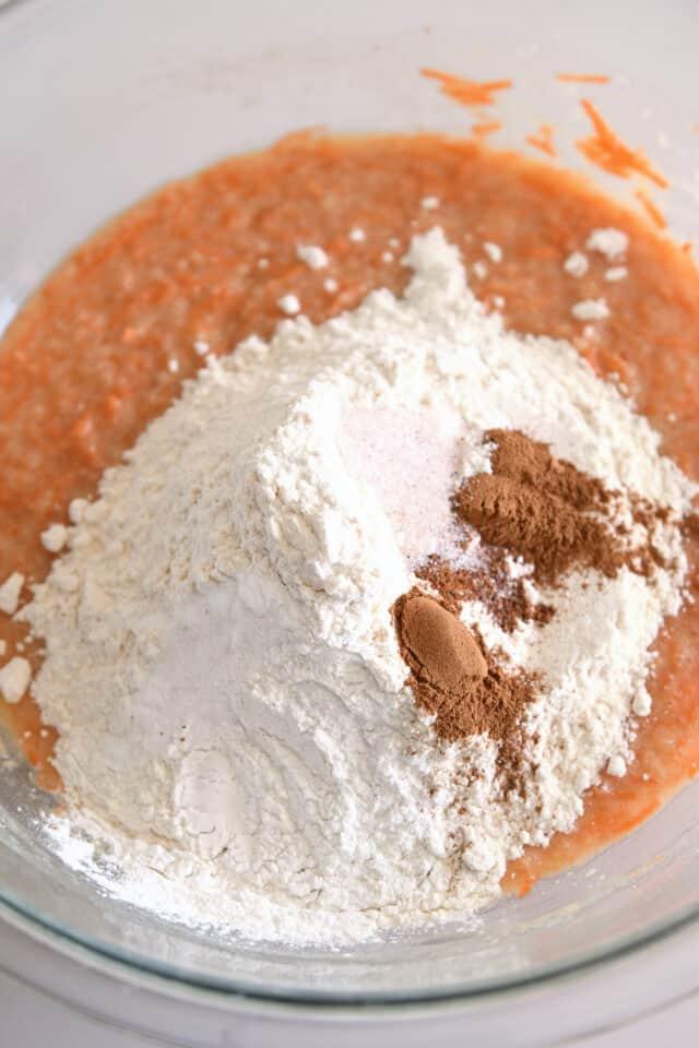 Flour, cinnamon, salt, and baking soda added to carrot cake batter in glass bowl.