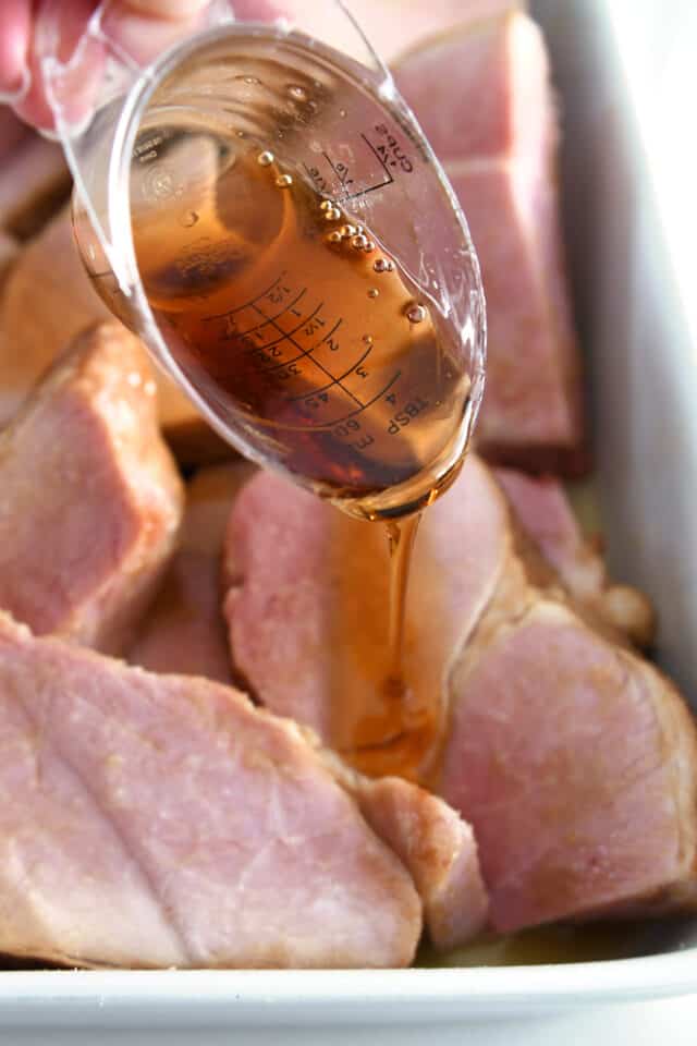 Pouring maple syrup over ham slices.