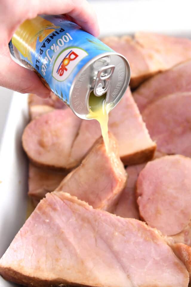 Pouring pineapple juice over ham slices.