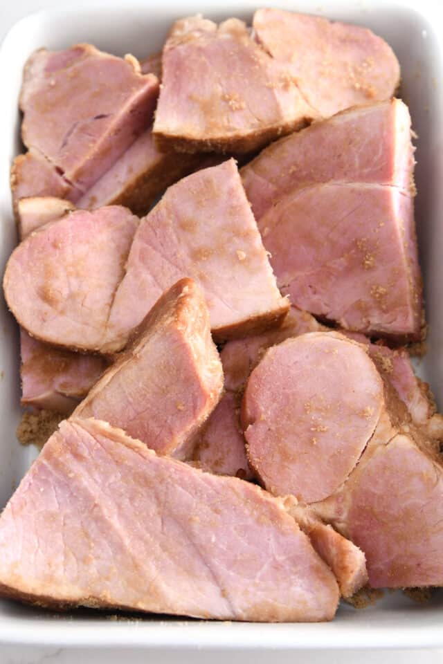 Brown sugar covering ham pieces in white dish.