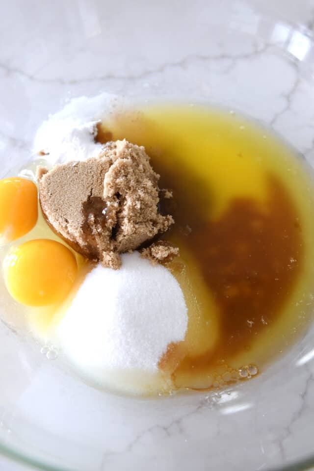 Glass bowl with white sugar, brown sugar, egg, egg yolk, and melted butter.