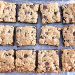 Twelve squares of cut chocolate chip cookie bars on white parchment paper.