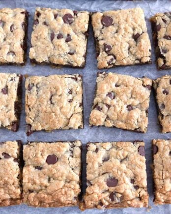 Twelve squares of cut chocolate chip cookie bars on white parchment paper.