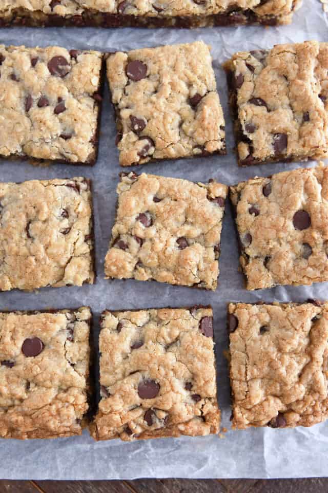 Nine cut squares of oatmeal chocolate chip cookie bars on white parchment paper.