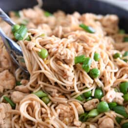 Tong grabbing scoop of ramen noodles with peas, ground turkey and green onions.