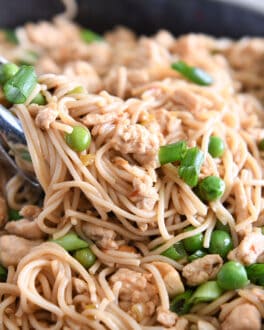 Tong grabbing scoop of ramen noodles with peas, ground turkey and green onions.