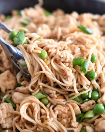 Tongs grabbing scoop of ramen noodles with peas and green onions.