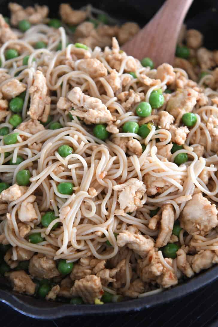 Stirring ramen noodles in cast iron skillet with frozen peas and ground turkey.