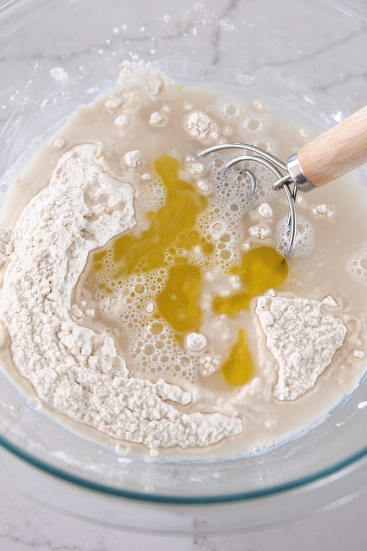 Flour, water, yeast and olive oil in glass bowl with Danish dough hook.