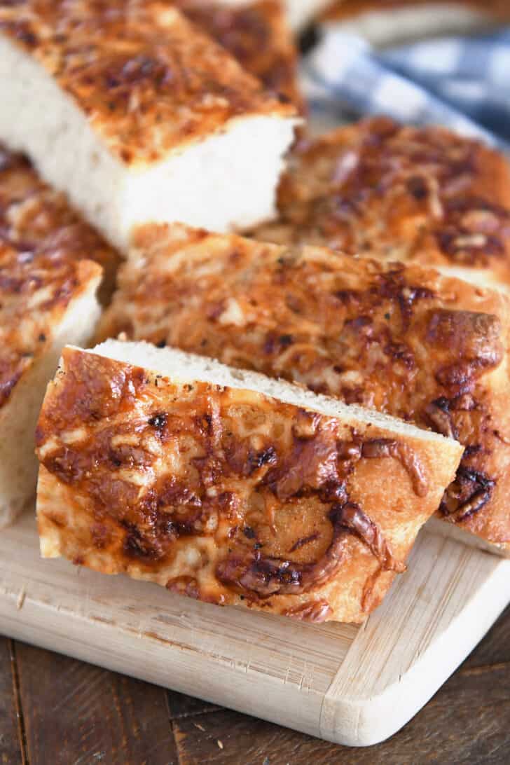 Three slices of Italian cheese bread on wood cutting board.