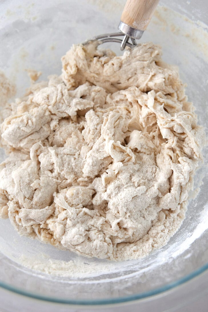 Glass bowl with bread dough ingredients mixed with Danish dough hook.