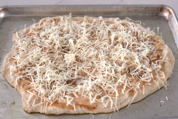 Mozzarella and parmesan cheese sprinkled on top of dough on half sheet pan.