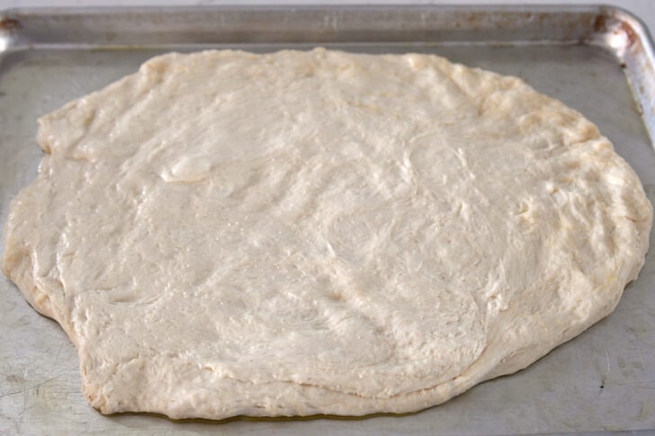 Dough pressed into rough oval shape on sheet pan.