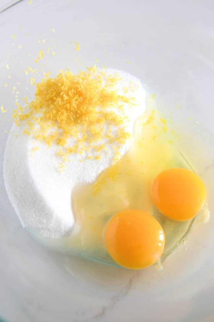 Gl، bowl with granulated sugar, lemon zest, and eggs.