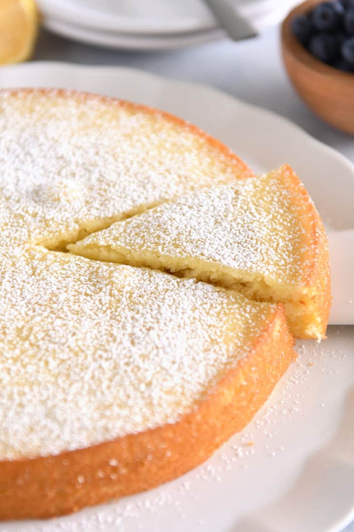 Triangle of olive oil cake dusted with powdered sugar cut out of whole cake.