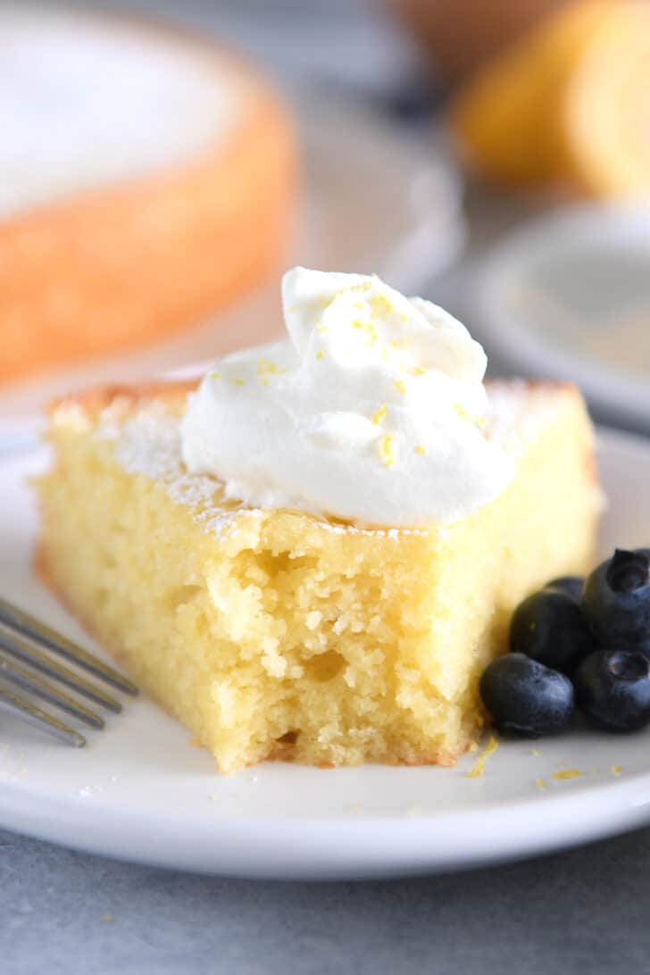 Triangle of olive oil cake on white plate with whipped cream and blueberries.