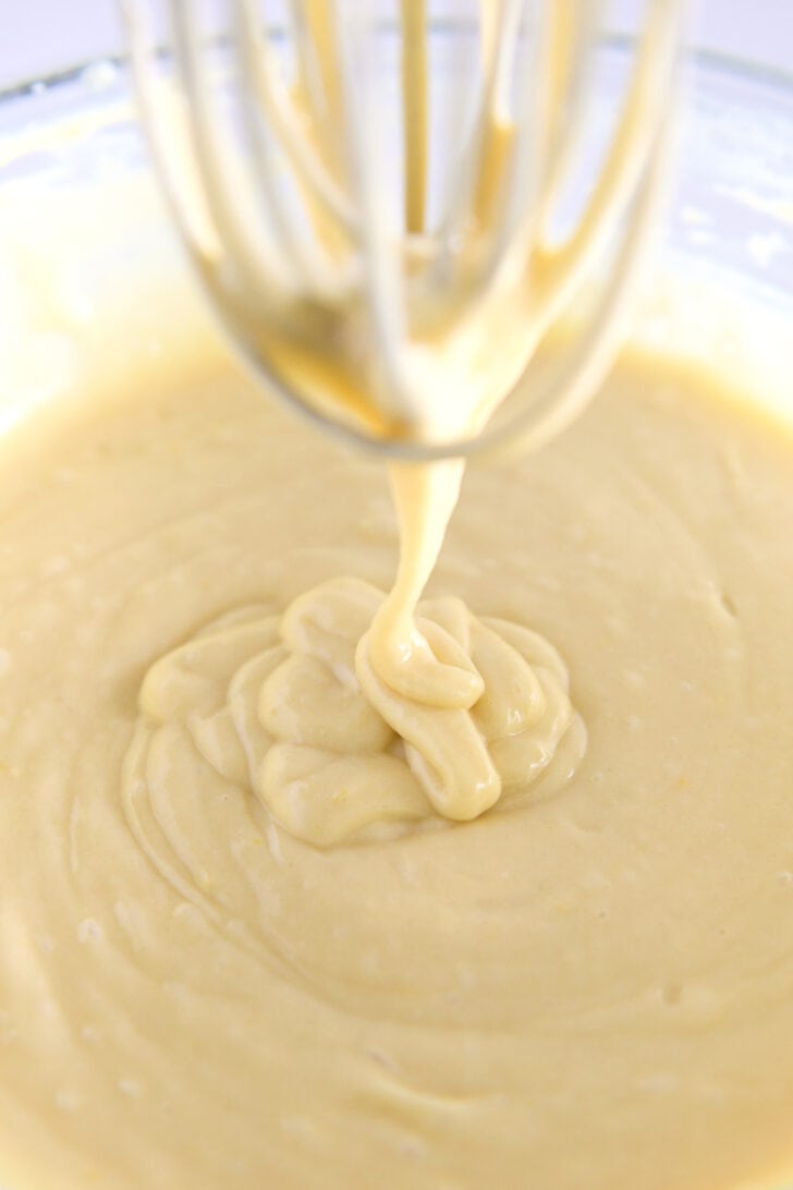 Whisk drizzling olive oil cake batter into glass bowl.