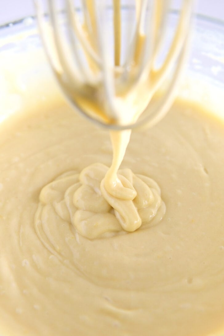 Whisk drizzling olive oil cake batter into gl، bowl.