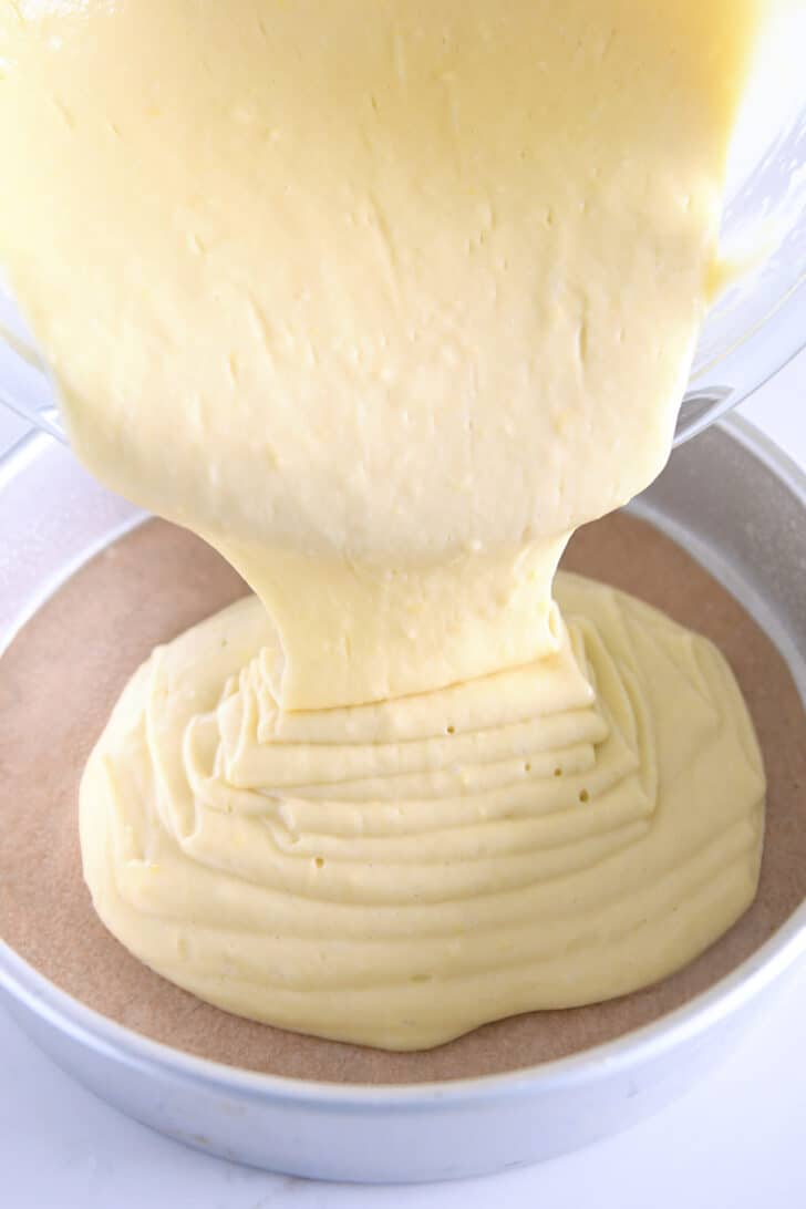 Pouring olive oil cake batter into parchment paper-lined round baking pan.