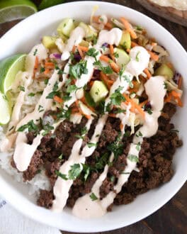 White bowl with rice, Korean beef, slaw, sauce, and lime wedges.