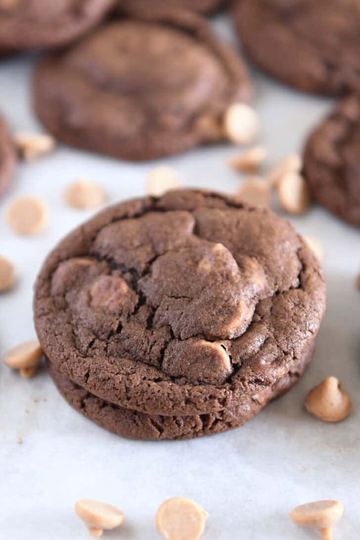 Two chocolate cookies with peanut butter chips stacked with a few peanut butter chips scattered around.