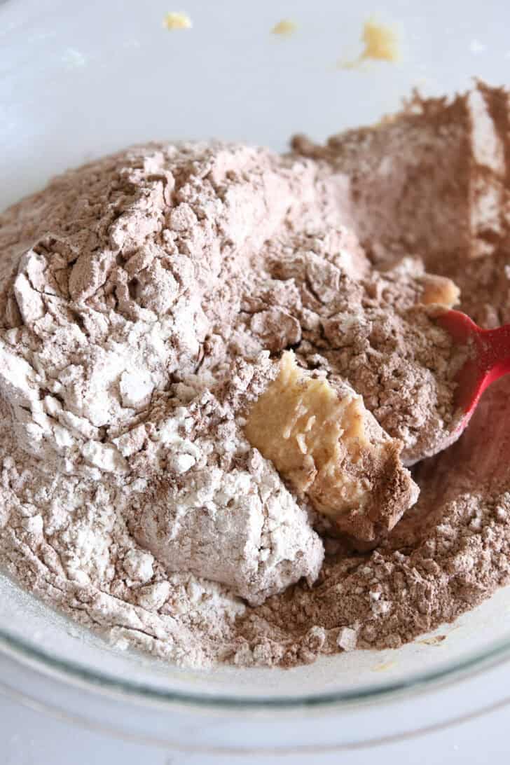 Glass bowl with cookie dough, flour, and cocoa powder.