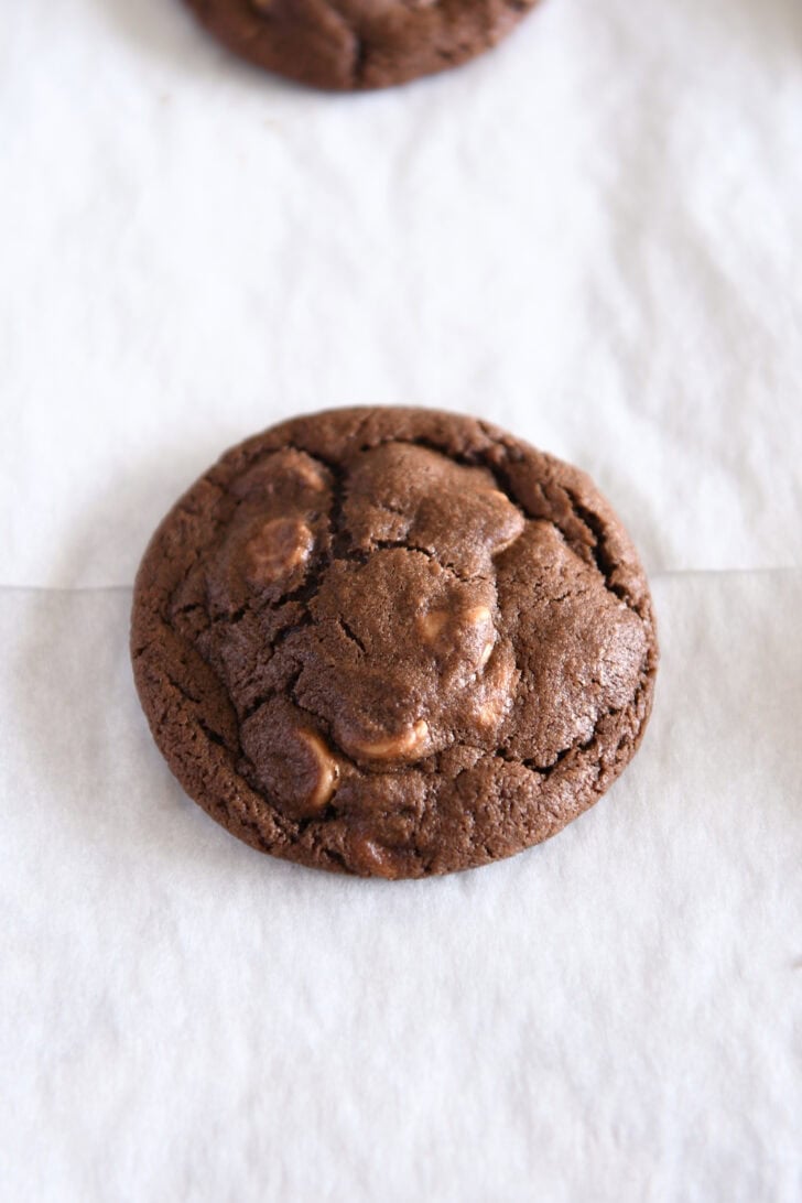 Baked chocolate cookie with peanut butter chips on parchment paper.