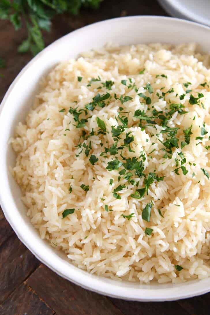 White bowl with fluffy rice and fresh parsley.