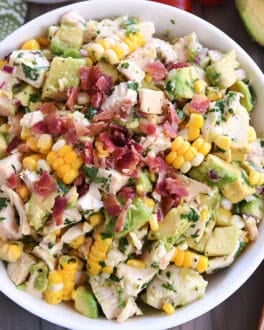 Top down view of a white bowl filled with diced chicken, diced avocado, chunks of fresh corn, and bacon bits.