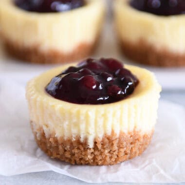 One mini cheesecake with huckleberry topping on piece of white parchment paper.