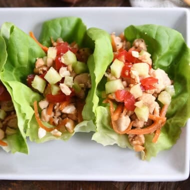Top down view of lettuce leaves full of a chicken vegetable mixture on a white plate.